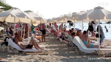希腊塞萨洛尼基(Thessaloniki)一个热带度假胜地的夏季海滩上挤满了海滩游客和度假者，他们在沙滩伞下放松